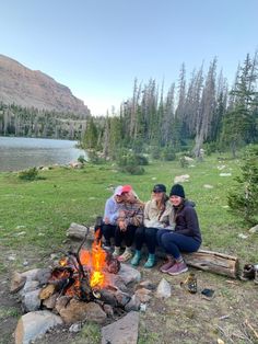 three people sitting around a campfire in the woods