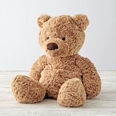 a brown teddy bear sitting on top of a wooden table next to a white wall