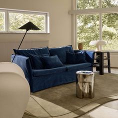 a living room with a blue couch and two lamps on the tables in front of large windows