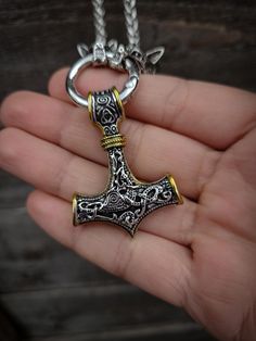 a hand holding a silver and gold necklace with an old style hammer pendant on it