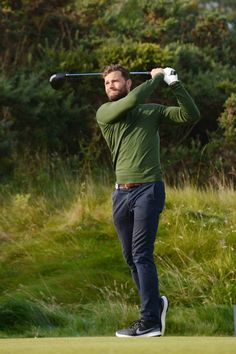 a man swinging a golf club on top of a green field