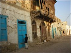 a man standing in front of a blue door on an old run down building with windows