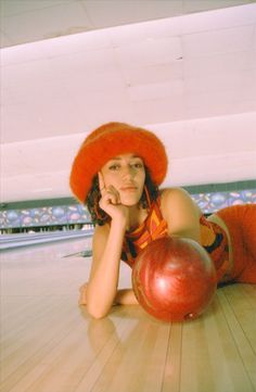 a woman laying on the floor next to a bowling ball and wearing a red hat