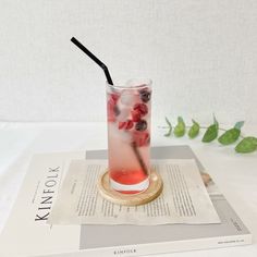 a drink with berries and ice sits on top of a book next to a plant