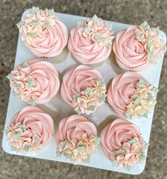 cupcakes decorated with pink frosting and flowers on a white tray, top view from above