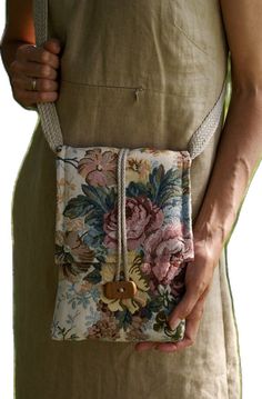 a woman is holding a small purse with flowers on the front and side, while she's wearing an apron