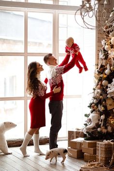 a man and woman holding a baby in front of a christmas tree