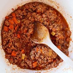 a wooden spoon in a white bowl filled with ground beef and carrots, topped with gravy