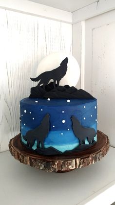 a blue and black cake with two wolf silhouettes on it's top, sitting on a wooden stand