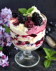 a trifle with berries and whipped cream in a glass dish next to purple flowers