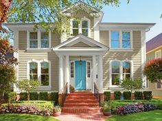 a house with blue front door and steps leading to the front door is surrounded by greenery