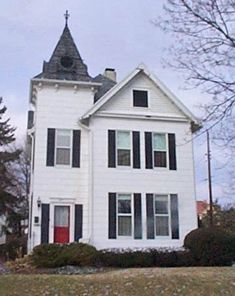 a large white house with a red door and black shutters on the front porch