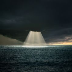 a black and white photo of the sun shining through dark clouds over the ocean on a cloudy day