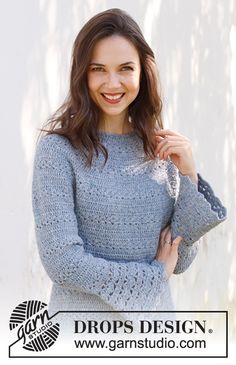 a woman standing next to a white wall wearing a blue sweater