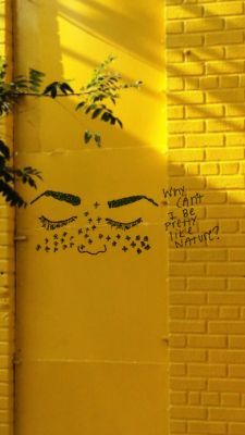 graffiti on the side of a yellow brick building with eyes drawn on it's face