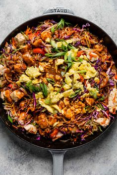 a skillet filled with chicken, cabbage and carrots on top of a table