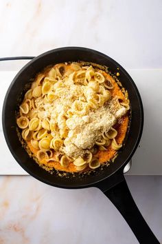 a skillet filled with pasta and cheese on top of a stovetop next to a white counter