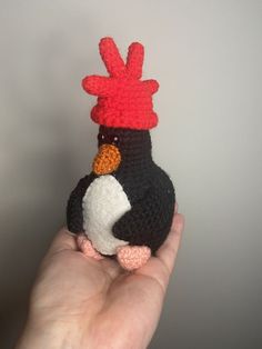 a small crocheted penguin with a red hat on it's head sitting in someones hand