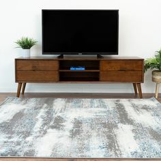 a flat screen tv sitting on top of a wooden entertainment center next to potted plants