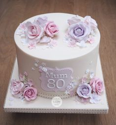 a white cake with pink and purple flowers on the top is decorated with an 80th birthday sign