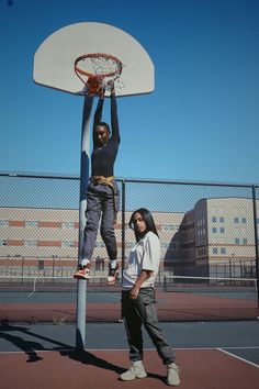 two people standing on a basketball court with a basket in the air and one person jumping up to dunk it