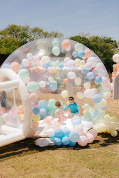 two children are playing in an inflatable ball on the grass with balloons all around them