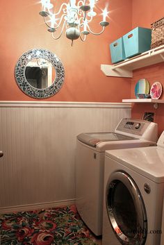 a washer and dryer in a small room with orange walls, rugs and chandelier