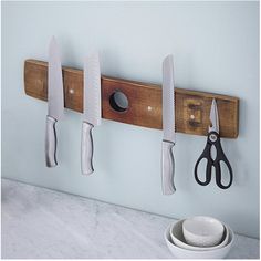 three knives are hanging on a wooden rack with two bowls and spoons next to it