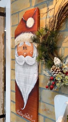 a wooden sign with a santa clause on it next to a brick wall and potted plants