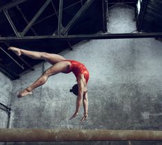 a woman in a red leotard is doing a handstand on a ledge