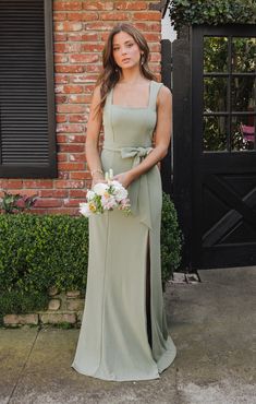 a woman standing in front of a brick building wearing a long green dress and holding a bouquet