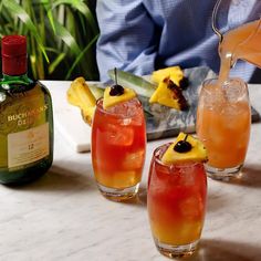 three glasses filled with drinks sitting on top of a table next to a bottle of alcohol