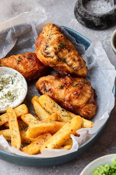 chicken and fries are served in a bowl with dipping sauce on the side, along with other food items