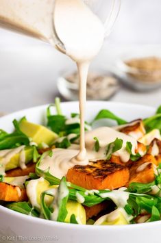 a salad with dressing being poured onto it in a white bowl on top of a table