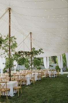 an outdoor tent with tables and chairs set up for a wedding reception in the grass