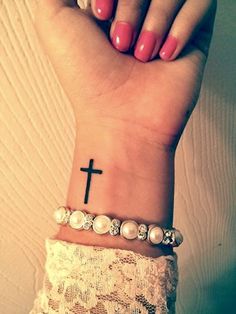 a woman's wrist with a cross tattoo on it and pearls around the wrist