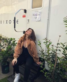 a woman sitting on top of a wooden bench next to a white trailer behind her