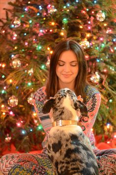 a woman sitting in front of a christmas tree with her dog