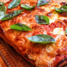 a close up of a pizza on a cooling rack with basil leaves and pepperoni