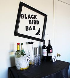 there is a black bird bar with bottles and glasses on the table next to it