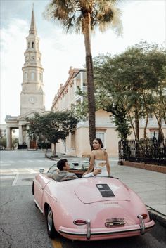 a woman sitting in the driver's seat of a pink sports car with a man standing next to it