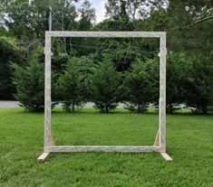 a wooden frame sitting on top of a lush green grass covered field next to trees