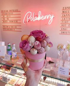 a person holding up a pink cup filled with lots of candies and flowers in front of a display case