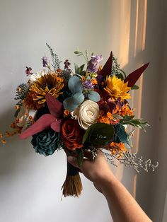 a hand holding a bouquet of flowers in front of a white wall with sunlight coming through the window