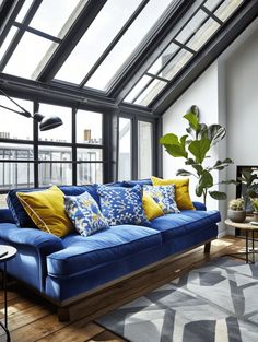 a living room with blue couches and yellow pillows on the floor next to a large window