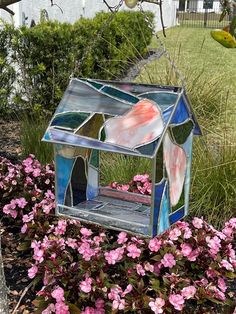 a birdhouse made out of stained glass sits in the grass next to pink flowers