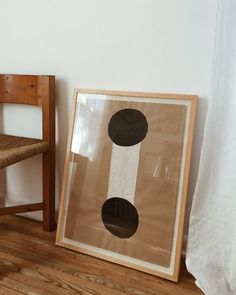 a wooden chair next to a painting on the floor in front of a white wall