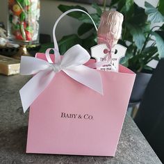 a pink gift bag with a white bow on the top that says baby & co