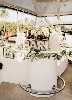 a white bar with flowers and candles on the table in front of it is decorated with greenery