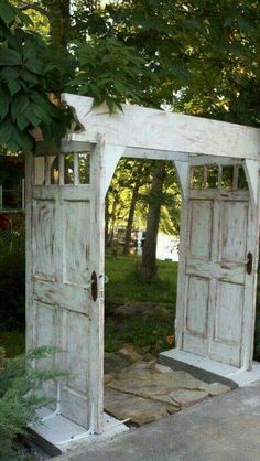 an old white wooden gate with two doors open in the middle of a garden area